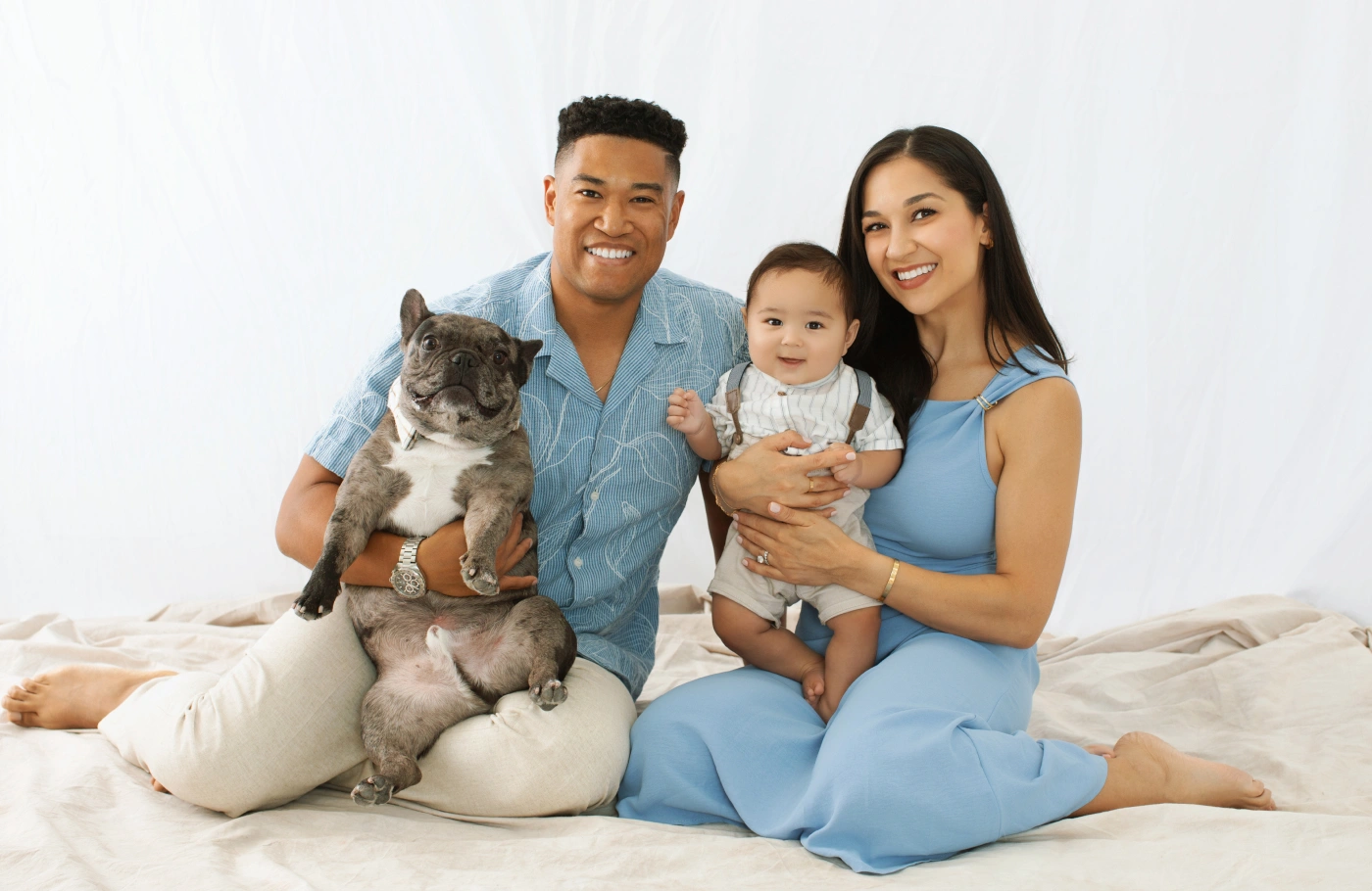 Family of four with cat sitting together on bed against white background